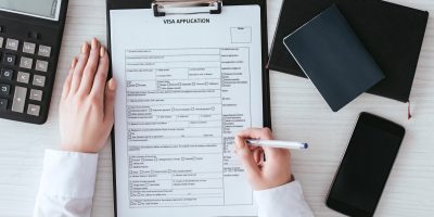 top-view-of-woman-holding-pen-near-document-with-visa-application-lettering-near-smartphone-with.jpg